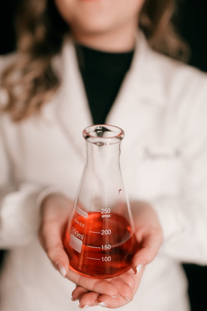 Home Close-up of a scientist holding an Erlenmeyer flask with red liquid in a lab setting.